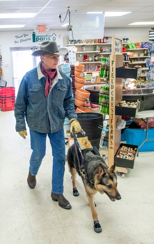 Man being guided by his German shepherd down the main aisle of a local farm store