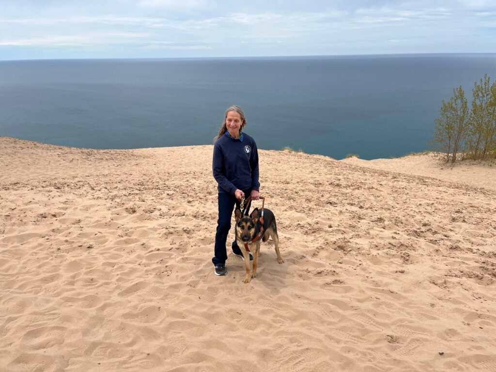 Sue and her Seeing Eye dog Kasey standing on a high sandy dune at Sleeping Bear Dunes National Lakeshore in Michigan.