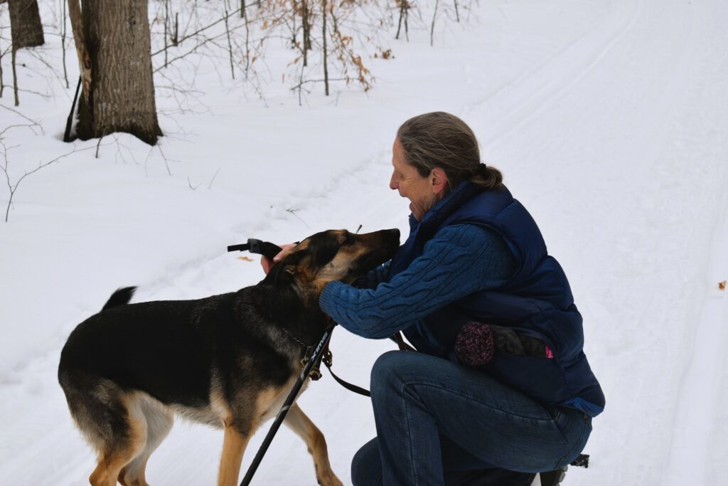 Sue crouching down to praise her Seeing Eye dog during a cross-country ski trip.